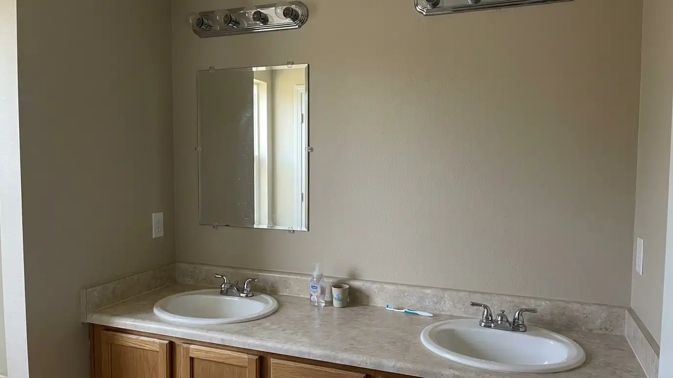 Before: a bathroom vanity wall with a small clipped-on builder mirror above a double vanity